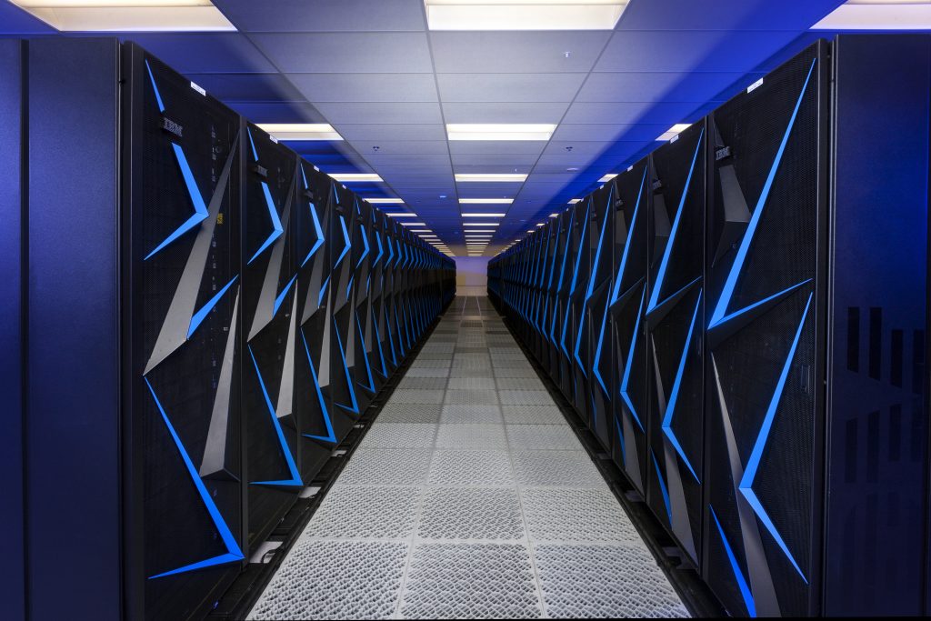 Long aisle between rows of black server racks with blue light panels in the Sierra supercomputer